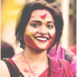 Vibrant portrait of a smiling woman with colorful face paint at Holi festival.